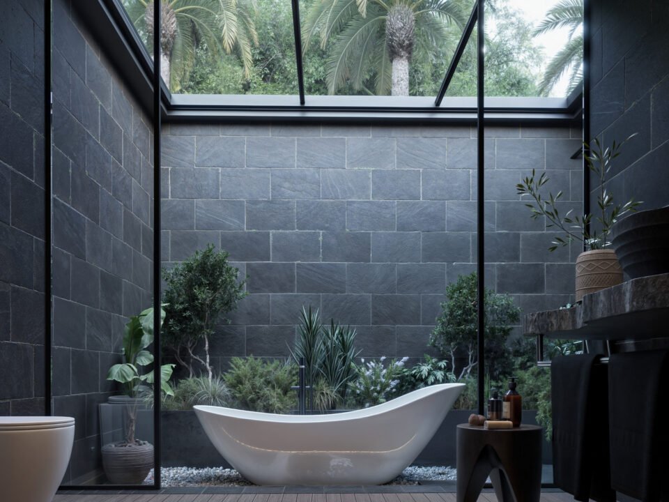 Modern open-air bathroom with dark stone walls and skylight